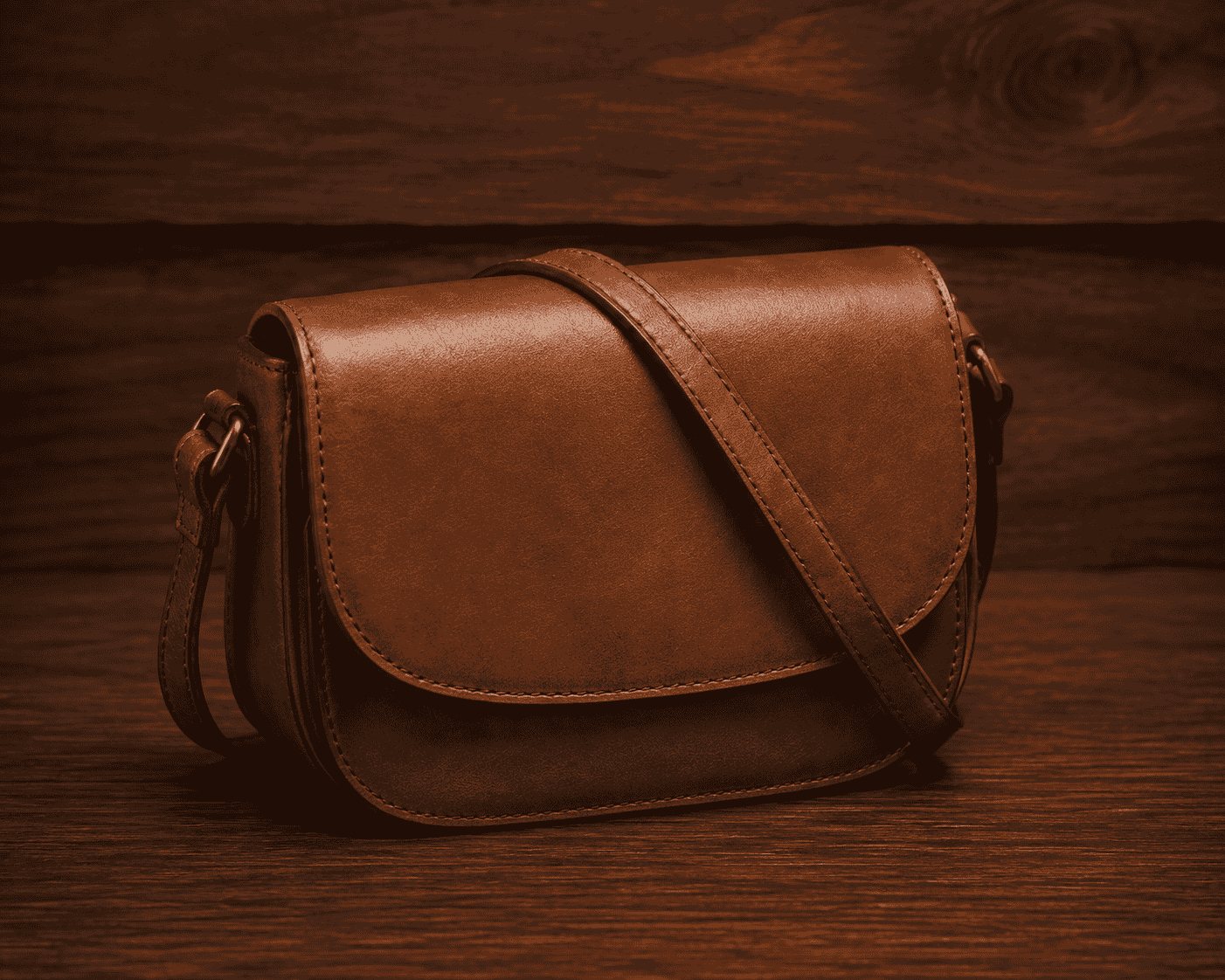 Tan leather flap crossbody bag showing curved saddle shape and shoulder strap
